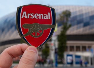 Arsenal reports £52.1m loss for 2022/23 amid revenue surge Man holding an Arsenal badge.