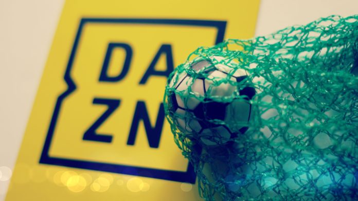 A yellow DAZN sign next to a football in a green net.