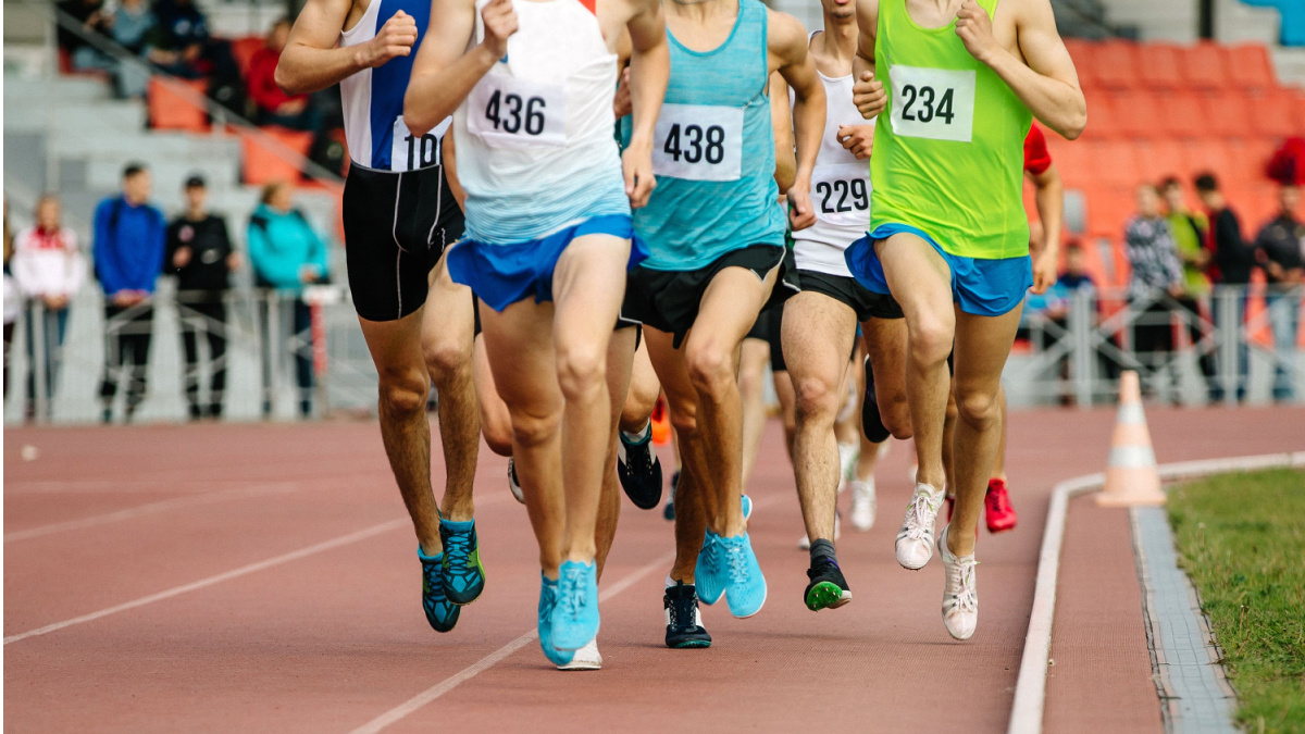 Group of male athletes running in a group round a track.