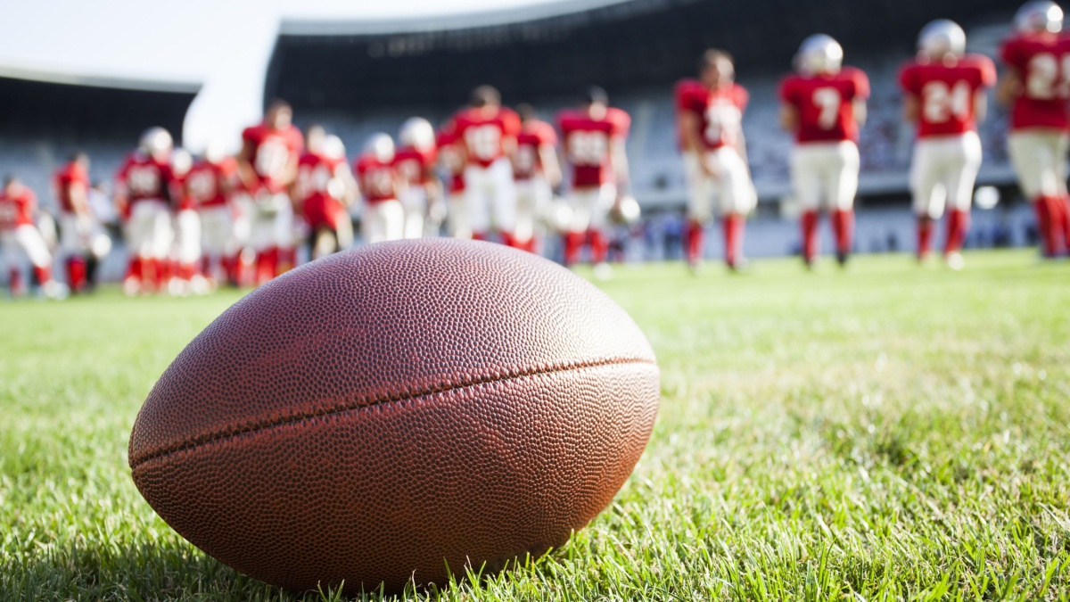 Close up of an American football on the field, players in the background.