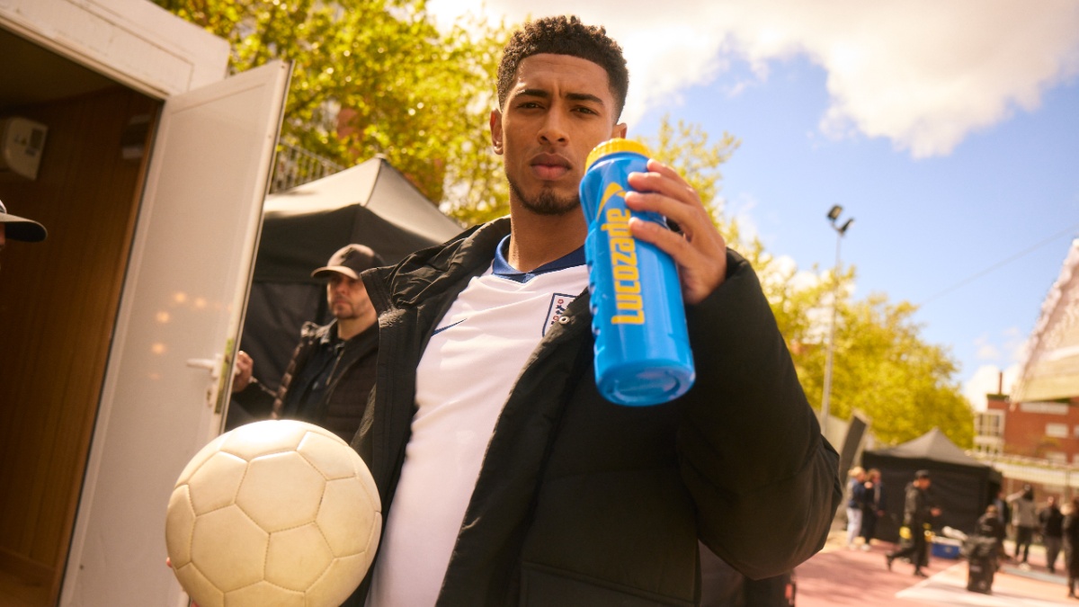 Jude Bellingham holding a football and a Lucozade branded bottle.