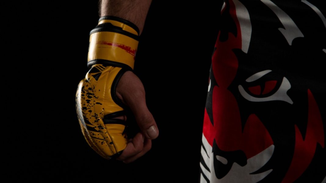 Mixed martial arts (MMA) fighter. Detail of the yellow glove with tiger pants on black background.
