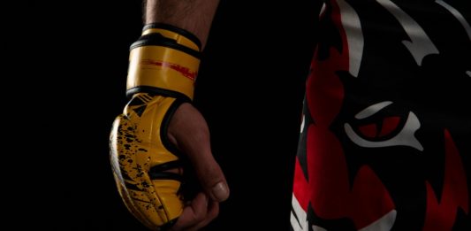Mixed martial arts (MMA) fighter. Detail of the yellow glove with tiger pants on black background.