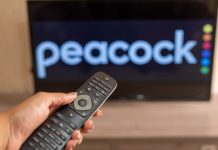 USL Super League chooses Peacock as official streaming platform A close-up of a hand holding a TV remote control seen in front of the Peacock logo.
