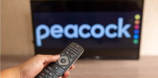 USL Super League chooses Peacock as official streaming platform A close-up of a hand holding a TV remote control seen in front of the Peacock logo.