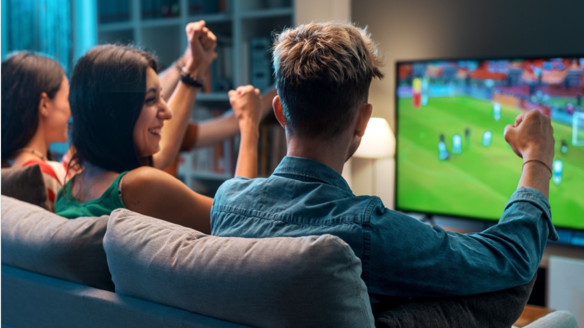 Group of young friends watching a football match on TV together and cheering for their team.
