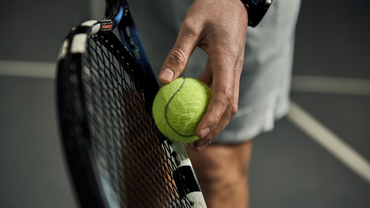 Close-up of male hand holding tennis ball and racket. Professional tennis player starting set.