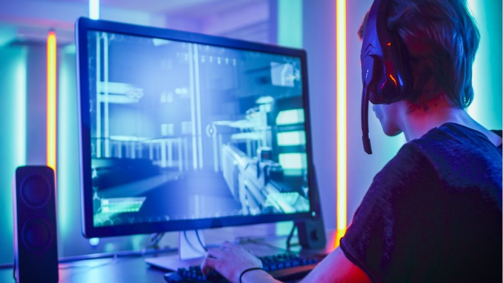 Shot of the Professional Gamer Playing in First-Person Shooter Online Video Game on His Personal Computer. Room Lit by Neon Lights in Retro Arcade Style. Online Cyber e-Sport Internet Championship.