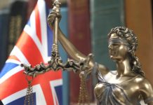 Sorare contests UKGC charges of unlicensed gambling Statue of Lady Justice with Bookshelf with Books and United Kingdom Flag Background. Tribunal and justice concept. Consultation with insurance lawyer and customer.