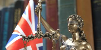 Sorare contests UKGC charges of unlicensed gambling Statue of Lady Justice with Bookshelf with Books and United Kingdom Flag Background. Tribunal and justice concept. Consultation with insurance lawyer and customer.