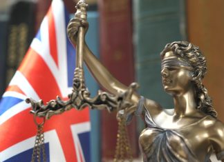 Sorare contests UKGC charges of unlicensed gambling Statue of Lady Justice with Bookshelf with Books and United Kingdom Flag Background. Tribunal and justice concept. Consultation with insurance lawyer and customer.