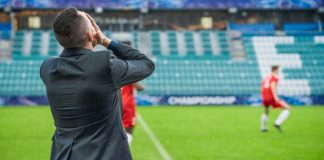 Lost trust? How the Football Manager delay impacts licensing Professional Soccer Football Match Championship on Stadium with Disappointed Coach Training Players. Teams Attacks, Plays in Pass. Major League Cup World Tournament Concept. Back View.