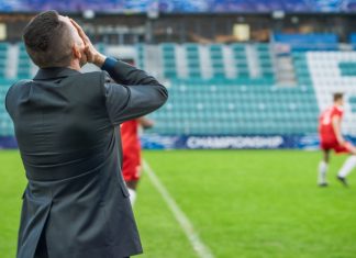 Lost trust? How the Football Manager delay impacts licensing Professional Soccer Football Match Championship on Stadium with Disappointed Coach Training Players. Teams Attacks, Plays in Pass. Major League Cup World Tournament Concept. Back View.