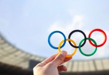 Olympics create career paths amid athlete pay debate Belo Horizonte, MG, Brazil - June 09, 2024. Illustrative editorial. A hand holds the Olympic rings with colors representing the continents, set against the backdrop of an Olympic stadium.