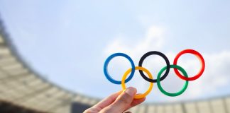 ANOC partners with Peak Sport to provide Olympic uniforms Belo Horizonte, MG, Brazil - June 09, 2024. Illustrative editorial. A hand holds the Olympic rings with colors representing the continents, set against the backdrop of an Olympic stadium.
