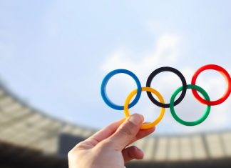 Olympics create career paths amid athlete pay debate Belo Horizonte, MG, Brazil - June 09, 2024. Illustrative editorial. A hand holds the Olympic rings with colors representing the continents, set against the backdrop of an Olympic stadium.