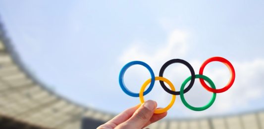 Belo Horizonte, MG, Brazil - June 09, 2024. Illustrative editorial. A hand holds the Olympic rings with colors representing the continents, set against the backdrop of an Olympic stadium.
