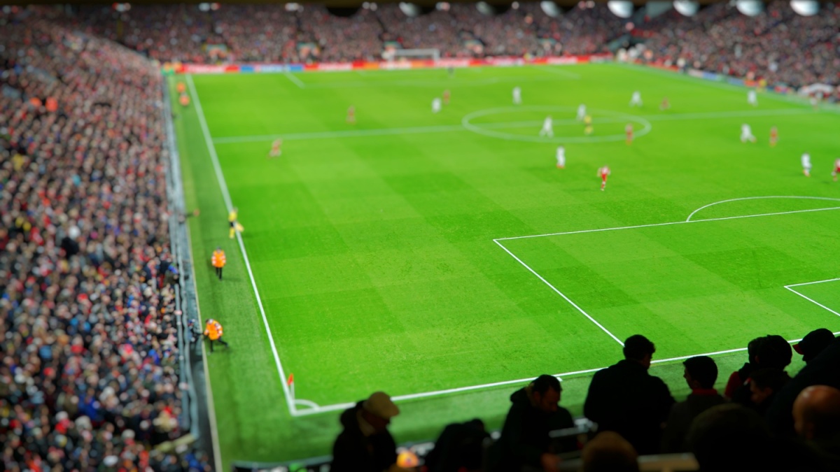 Blurred background of football players playing and soccer fans in match day on beautiful green field with sport light at the stadium. Sports,Athlete,People Concept.Anfield,Mercyside,Liverpool,UK.