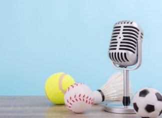 iGaming Daily: Insider Sport’s highlights and predictions Concept sports commentator : The retro microphone put on the wooden table with football or soccer , tennis ball , baseball and shuttlecock isolated on blue background.