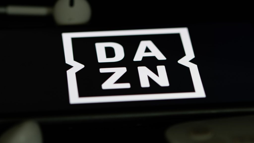 Rheinbach, Germany 5 June 2021, The logo of the streaming service "DAZN" on the screen of a smartphone with white headphones and a remote control.