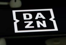DAZN targets $5bn revenue goal amid streaming battle Rheinbach, Germany 5 June 2021, The logo of the streaming service "DAZN" on the screen of a smartphone with white headphones and a remote control.
