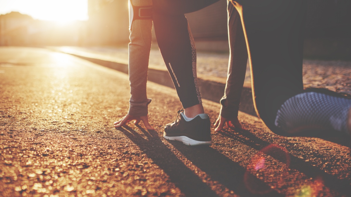 Athlete woman in running start pose on the city street. Sport tight clothes. Bright sunset, blurry background. Horizontal