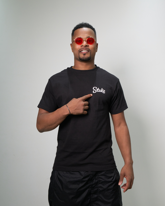 Patrice Evra pointing to Stake logo on a black t-shirt. 