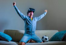 Burnley’s VR broadcast signals football’s next commercial goldmine young happy and excited gamer man using VR virtual reality goggles headgear set playing football simulation game celebrating scoring goal at home sofa couch enjoying 3D glasses fun experience.