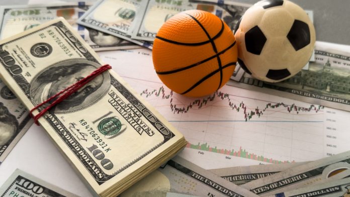 Image of a small toy basketball and football on top of a wad of dollar bills, representative of spot fixing