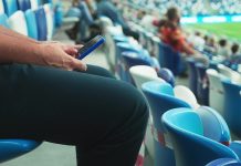 Meta emerges as top platform for sports fans online A man sits on the stadium stand and surfing social media on his smart phone during a football or soccer match. Mass event during coronavirus quarantine. Close-up of hands. High quality 4k footage