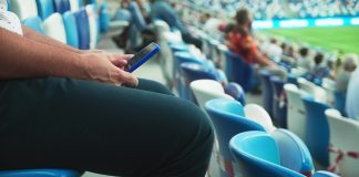 Meta emerges as top platform for sports fans online A man sits on the stadium stand and surfing social media on his smart phone during a football or soccer match. Mass event during coronavirus quarantine. Close-up of hands. High quality 4k footage