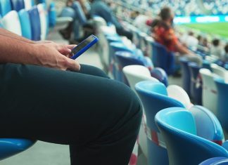 Meta emerges as top platform for sports fans online A man sits on the stadium stand and surfing social media on his smart phone during a football or soccer match. Mass event during coronavirus quarantine. Close-up of hands. High quality 4k footage