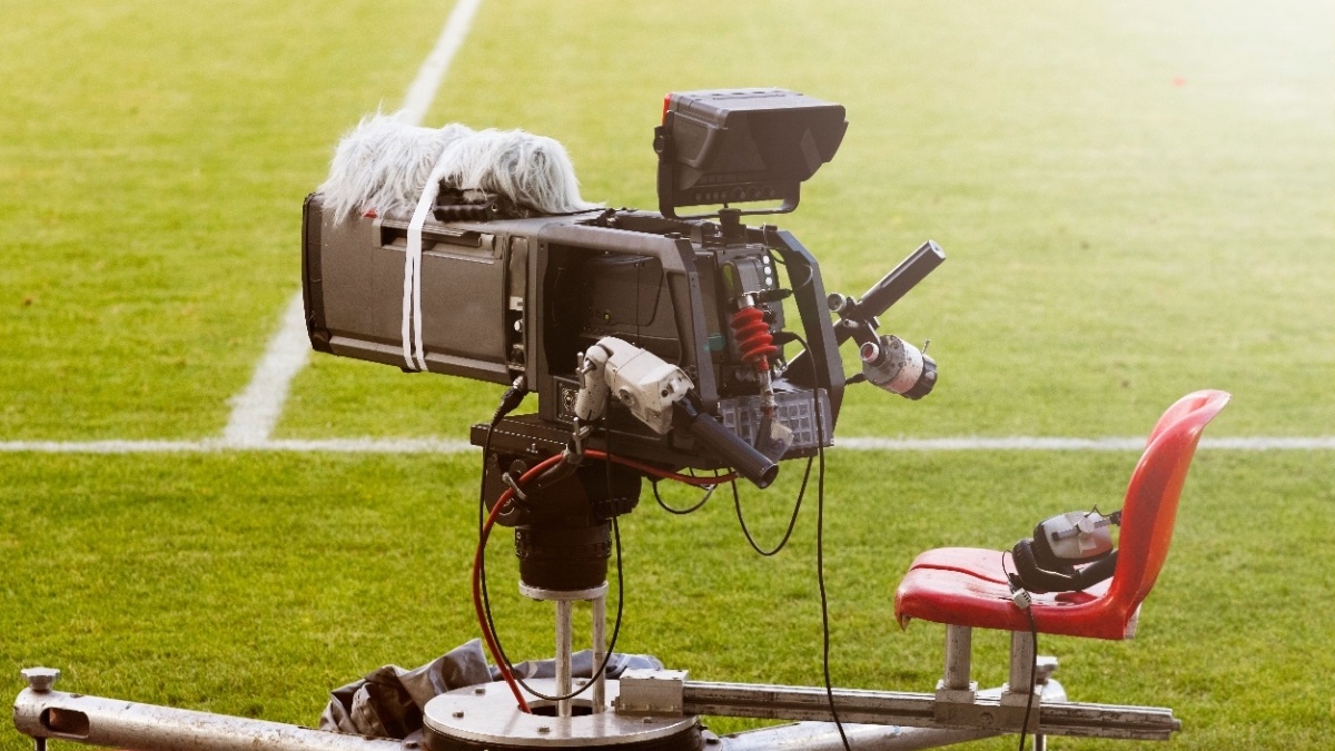 Television broadcast camera shooting at a sunny football game.