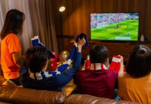 How interactive overlays are changing sports streaming Group of Asian people friends sit on sofa watching and cheering football or soccer games competition on TV together at home.Happy man and woman sport fans celebrating sport team victory sports match.