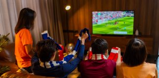 How interactive overlays are changing sports streaming Group of Asian people friends sit on sofa watching and cheering football or soccer games competition on TV together at home.Happy man and woman sport fans celebrating sport team victory sports match.