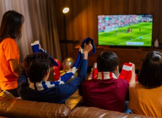 How interactive overlays are changing sports streaming Group of Asian people friends sit on sofa watching and cheering football or soccer games competition on TV together at home.Happy man and woman sport fans celebrating sport team victory sports match.
