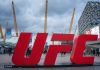 Former UFC fighter called out for illegal gambling sponsorship London, UK. April 2, 2025. The O2 Arena in London features its iconic dome and yellow masts, a red UFC sign in the foreground, modern buildings, and a cloudy sky above.