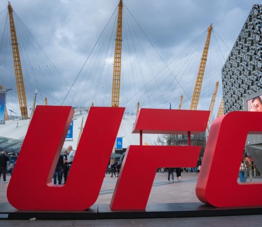 Former UFC fighter called out for illegal gambling sponsorship London, UK. April 2, 2025. The O2 Arena in London features its iconic dome and yellow masts, a red UFC sign in the foreground, modern buildings, and a cloudy sky above.