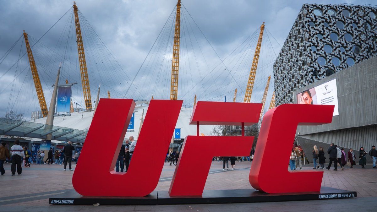 London, UK. April 2, 2025. The O2 Arena in London features its iconic dome and yellow masts, a red UFC sign in the foreground, modern buildings, and a cloudy sky above.
