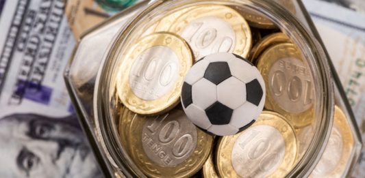 Symbolic soccer ball, 100 KZT coins and 100 US dollar bills.