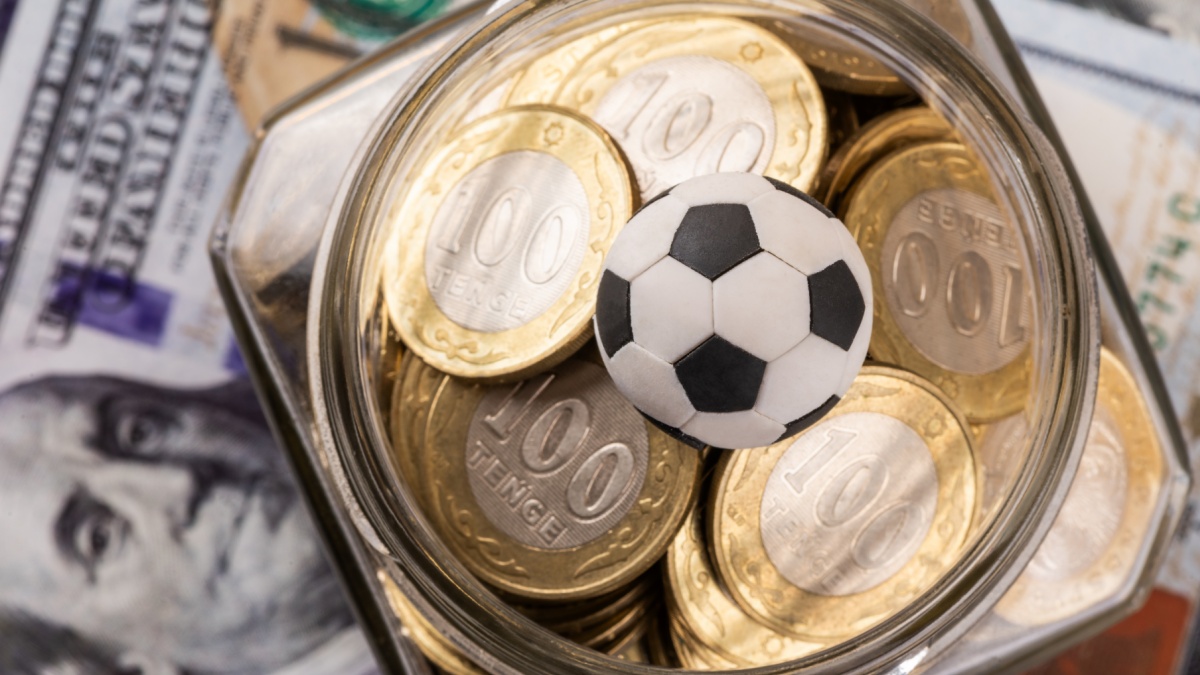 Symbolic soccer ball, 100 KZT coins and 100 US dollar bills.