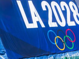 The Olympics clock is ticking toward irrelevance 2024-11-20 Los Angeles USA A promotional banner for the LA 2028 Olympics featuring the Olympic rings, displayed on a blue background with a green fence below.