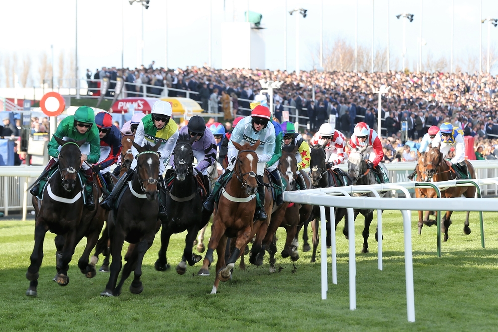 AINTREE RACECOURSE, LIVERPOOL, UK : 8 April 2022 : Horses and jockeys gallop round the bend at the end of the home straight in front of packed Grandstands during the Grand National Festival at Aintree