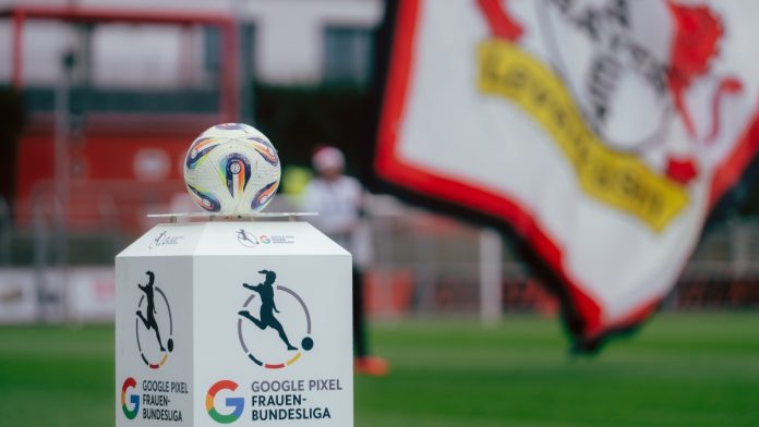 06.12.2025, Leverkusen, Google Pixel Frauen Bundesliga, Bayer 04 Leverkusen - RB Leipzig, Germany Ein Google Pixel Frauen Bundesliga Ball liegt auf einem Podest vor dem Spiel, im Hintergrund eine Bayer 04 Leverkusen Fahne.