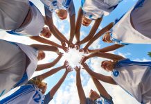 Women’s sport has won visibility – now it must win value Women basketball team shows solidarity by forming a supportive circle beneath a clear sky. Concept of shared focus, youth rituals in sport, fitness education, marketing for athletic brands.