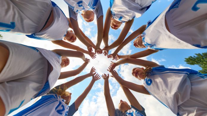 Women's-sport- Women basketball team shows solidarity by forming a supportive circle beneath a clear sky. Concept of shared focus, youth rituals in sport, fitness education, marketing for athletic brands.