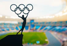 ‘I don’t believe in paying athletes’, says IOC President Statue of athletics Woman holding above head olympic circle. Modern Olympic Stadium in Background. Sport photo for Summer olympic Game in Paris 2024.