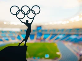 ‘I don’t believe in paying athletes’, says IOC President Statue of athletics Woman holding above head olympic circle. Modern Olympic Stadium in Background. Sport photo for Summer olympic Game in Paris 2024.