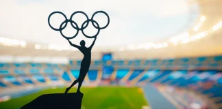 ‘I don’t believe in paying athletes’, says IOC President Statue of athletics Woman holding above head olympic circle. Modern Olympic Stadium in Background. Sport photo for Summer olympic Game in Paris 2024.