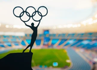 ‘I don’t believe in paying athletes’, says IOC President Statue of athletics Woman holding above head olympic circle. Modern Olympic Stadium in Background. Sport photo for Summer olympic Game in Paris 2024.